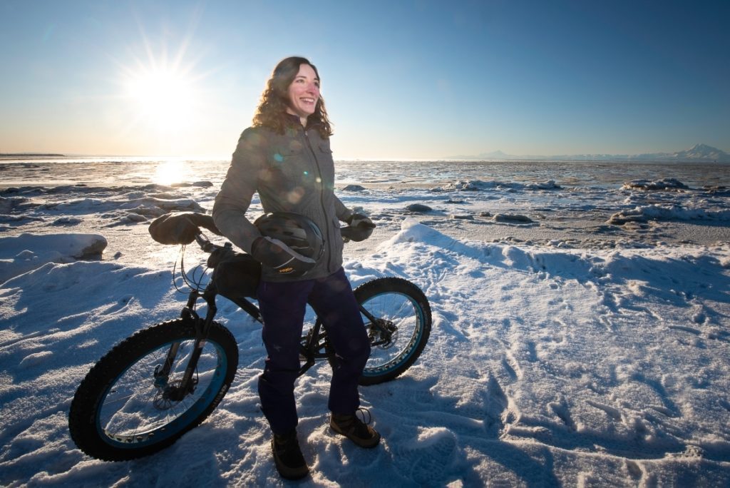 Woman on beach in winter standing next to a bike